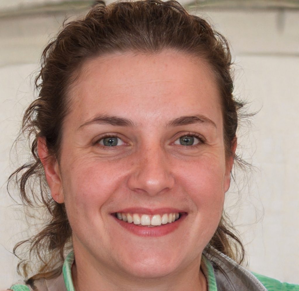 A woman with wavy brown hair, green eyes, and a bright smile is looking at the camera. She is wearing a light green collared shirt and is photographed in a well-lit indoor setting.